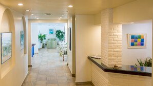 A hotel reception area with a reception desk, framed artwork on the walls, and a tiled floor. - Hotel Doce Mar (Búzios)