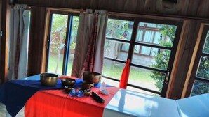 A room with a table set with meditation bowls and a remote control, large windows with curtains, and a view of greenery outside. - Alecrim Pousada (Garopaba)