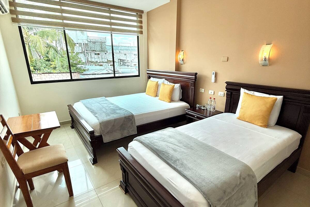 A hotel room with two beds, a wooden desk, and a chair.
