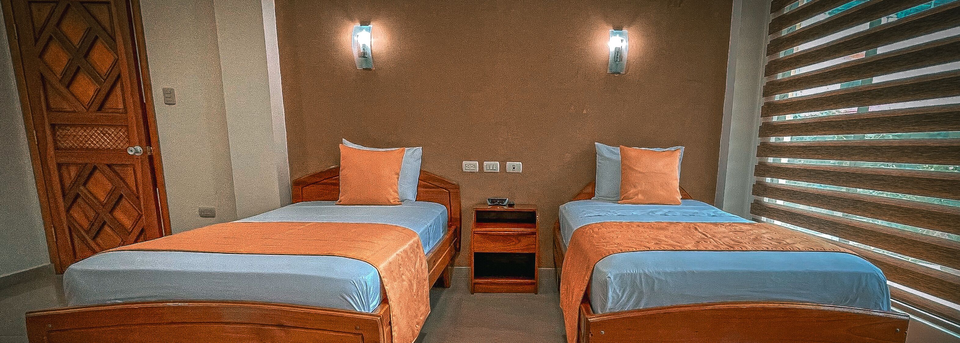 Una habitación con dos camas, una puerta de madera y una pared con persianas horizontales.