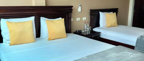 A hotel room with two beds, each with white linens and yellow pillows. There are bedside tables with water bottles and a phone.