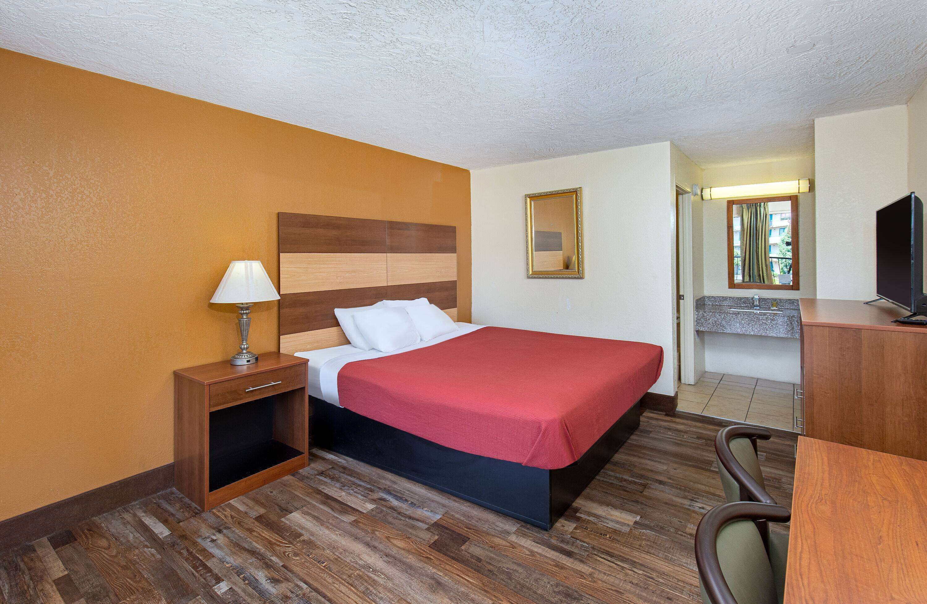 Une chambre d’hôtel avec un lit, une table de chevet avec une lampe, une télévision et une vue sur l’extérieur par une fenêtre.