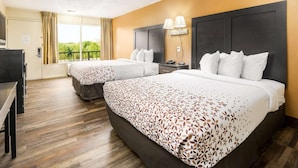 A hotel room with two beds, a desk, and a window with curtains. - Americana Inn, a Travelodge by Wyndham (Pigeon Forge)