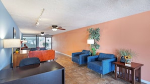 A modern living room with a dark wooden desk, blue armchairs, and a small table with a plant. - Americana Inn, a Travelodge by Wyndham (Pigeon Forge)