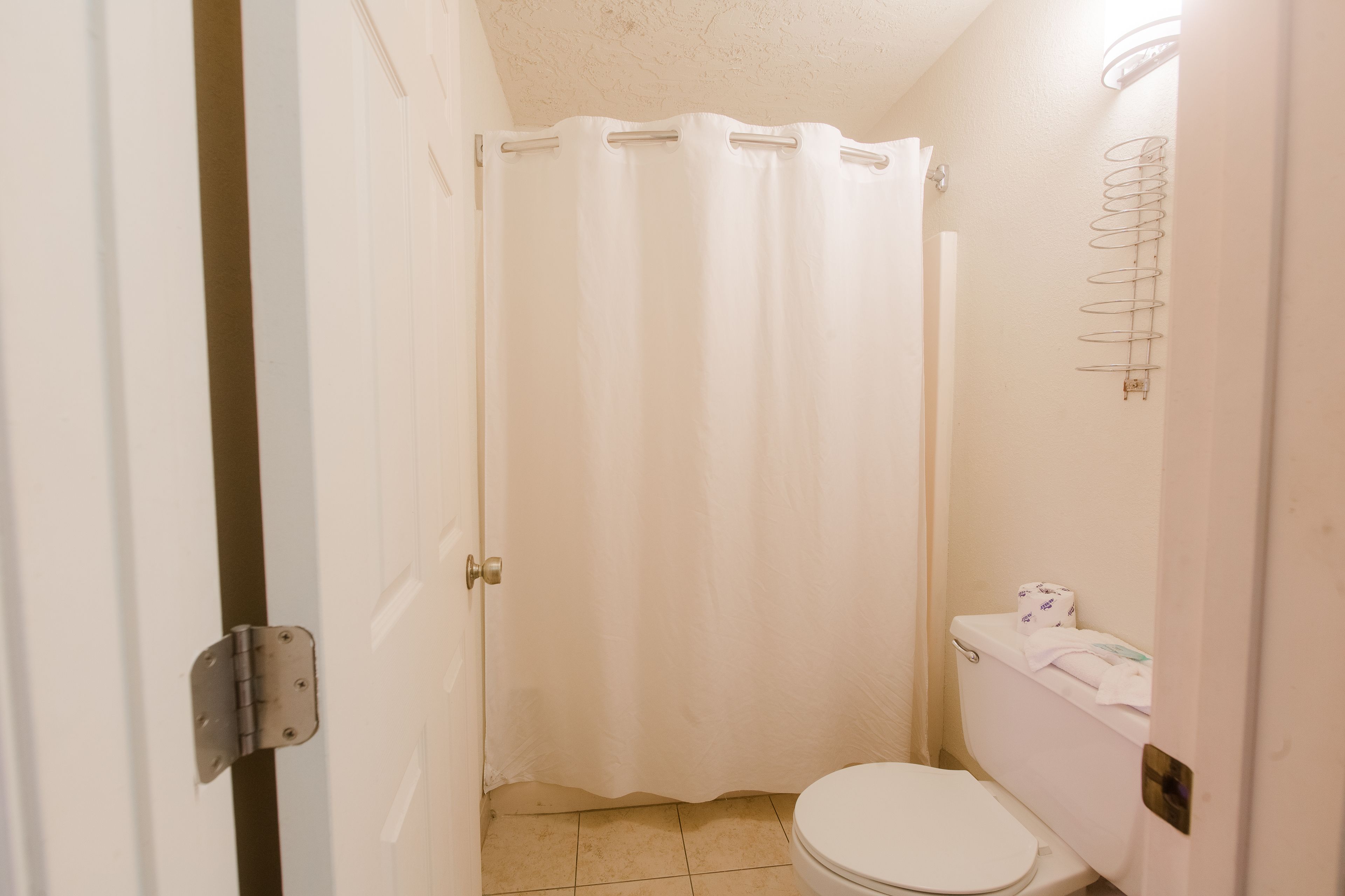 Une petite salle de bain propre, équipée de toilettes, d’un rideau de douche et d’un porte-rouleau de papier toilette.