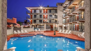A swimming pool with lounge chairs and a building with multiple balconies in the background. - Americana Inn, a Travelodge by Wyndham (Pigeon Forge)