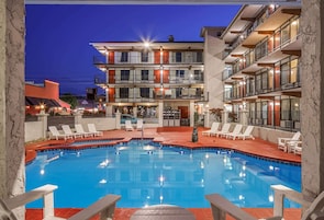 A swimming pool with lounge chairs and a building with multiple balconies in the background.
