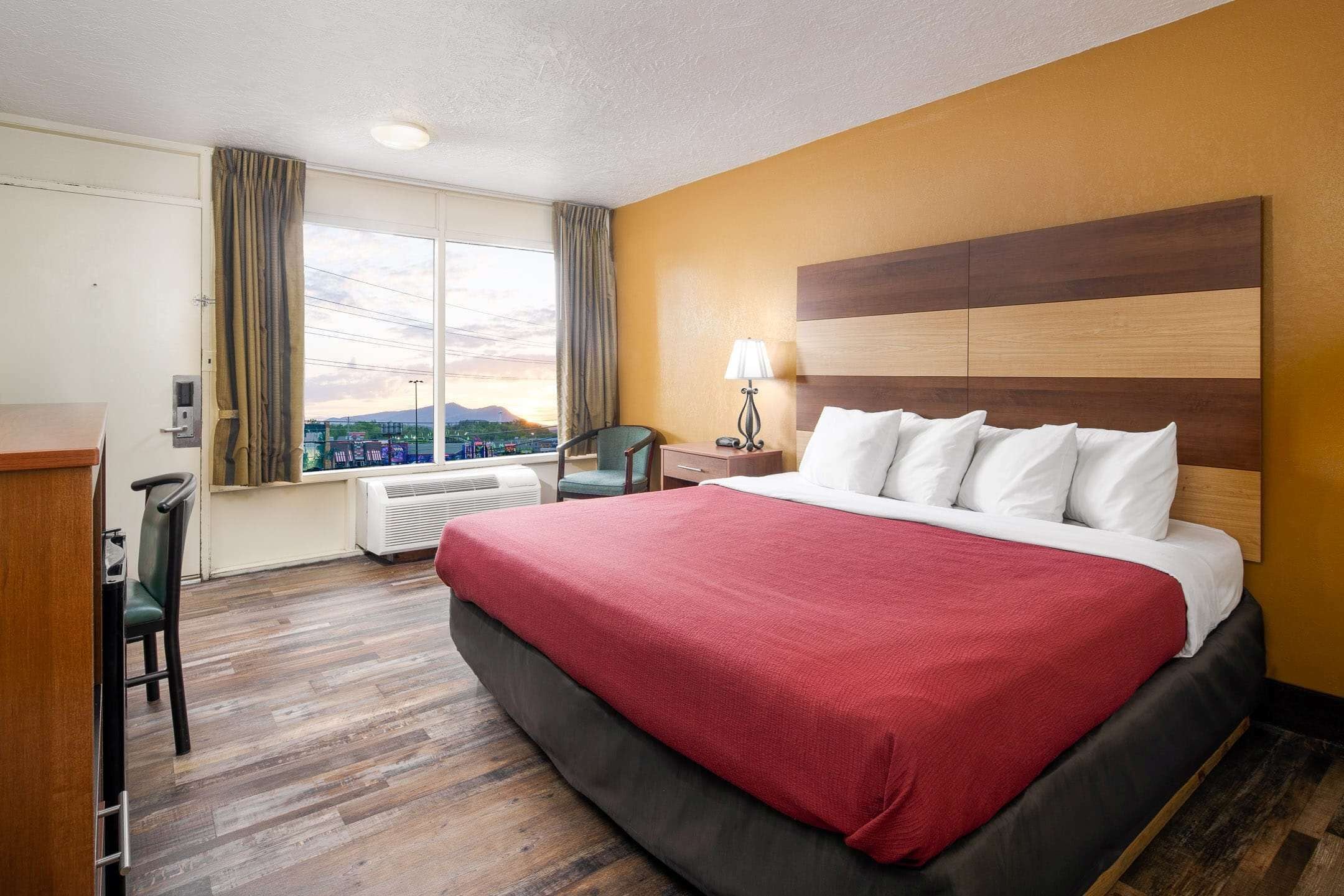A hotel room with a large bed, a desk, a chair, a nightstand, and a window with a view of the city.