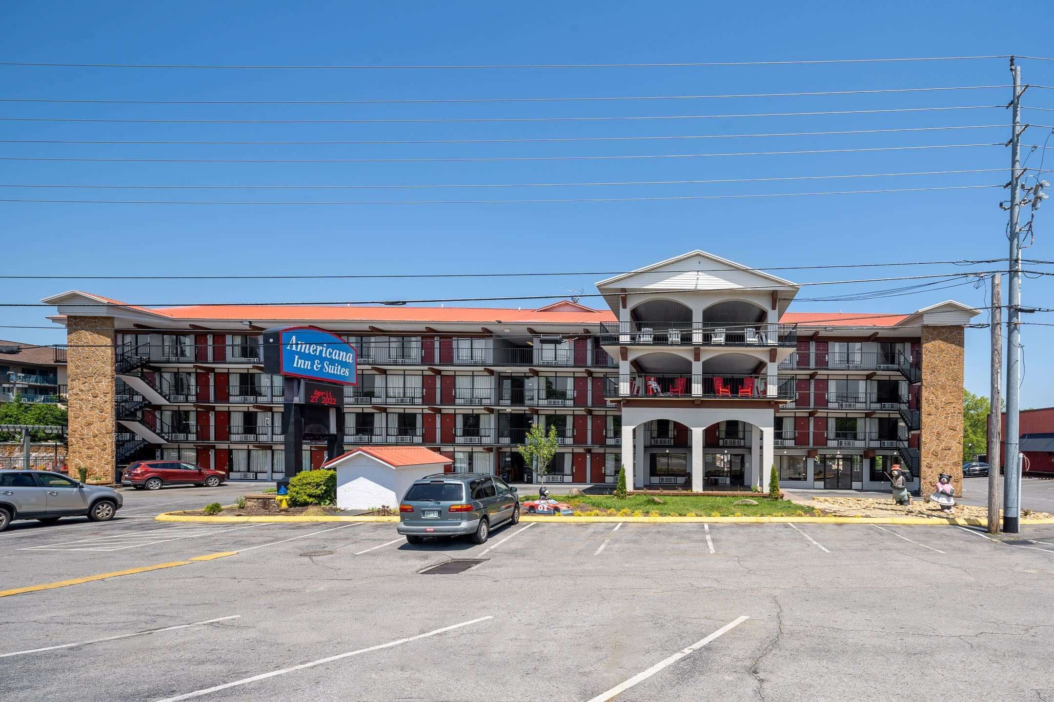 A multi-story hotel with a red roof, a central entrance with a balcony, and a parking lot in front.
