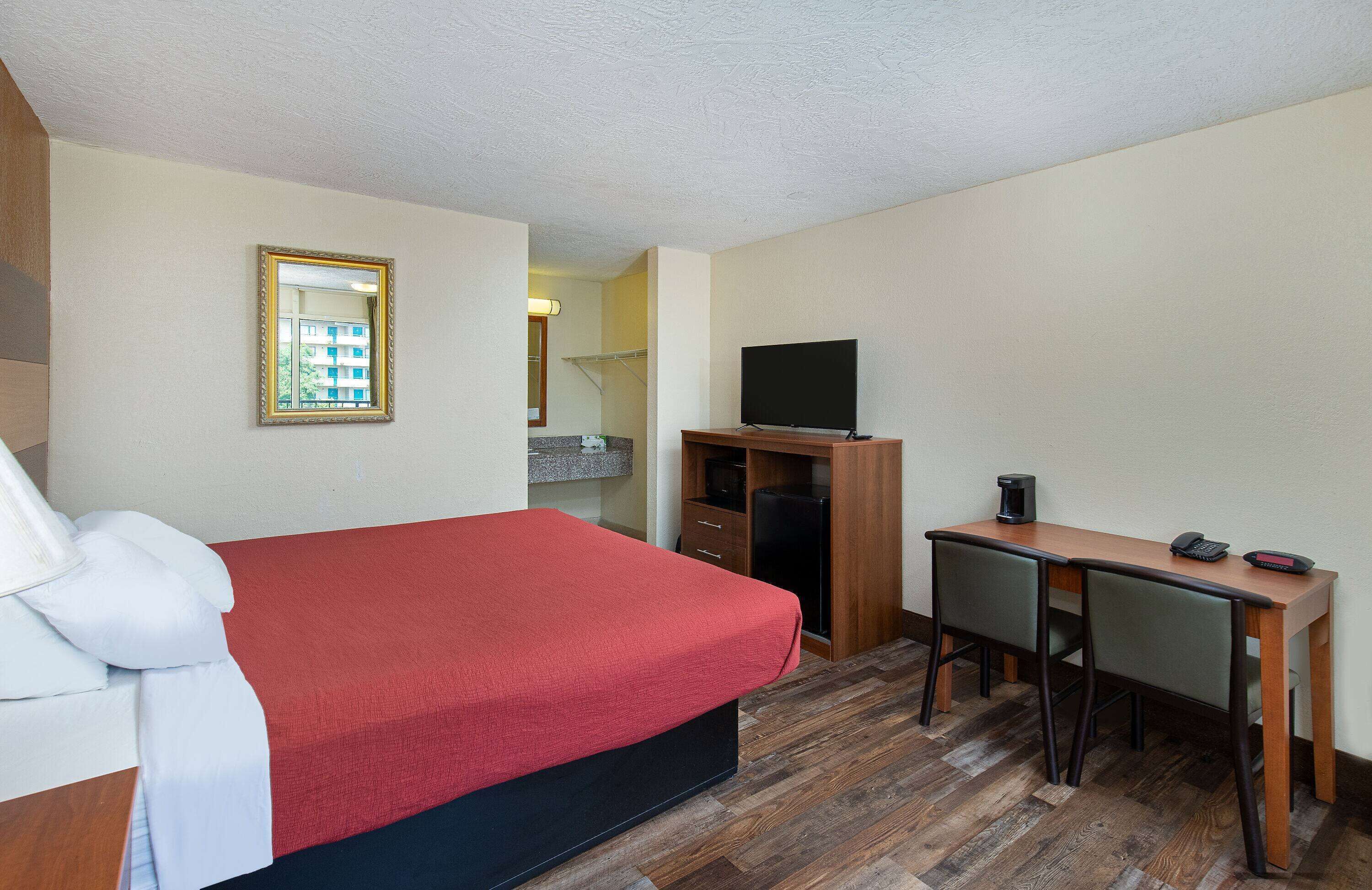 Habitación de hotel con cama, escritorio, silla, televisor y un pequeño rincón de cocina.