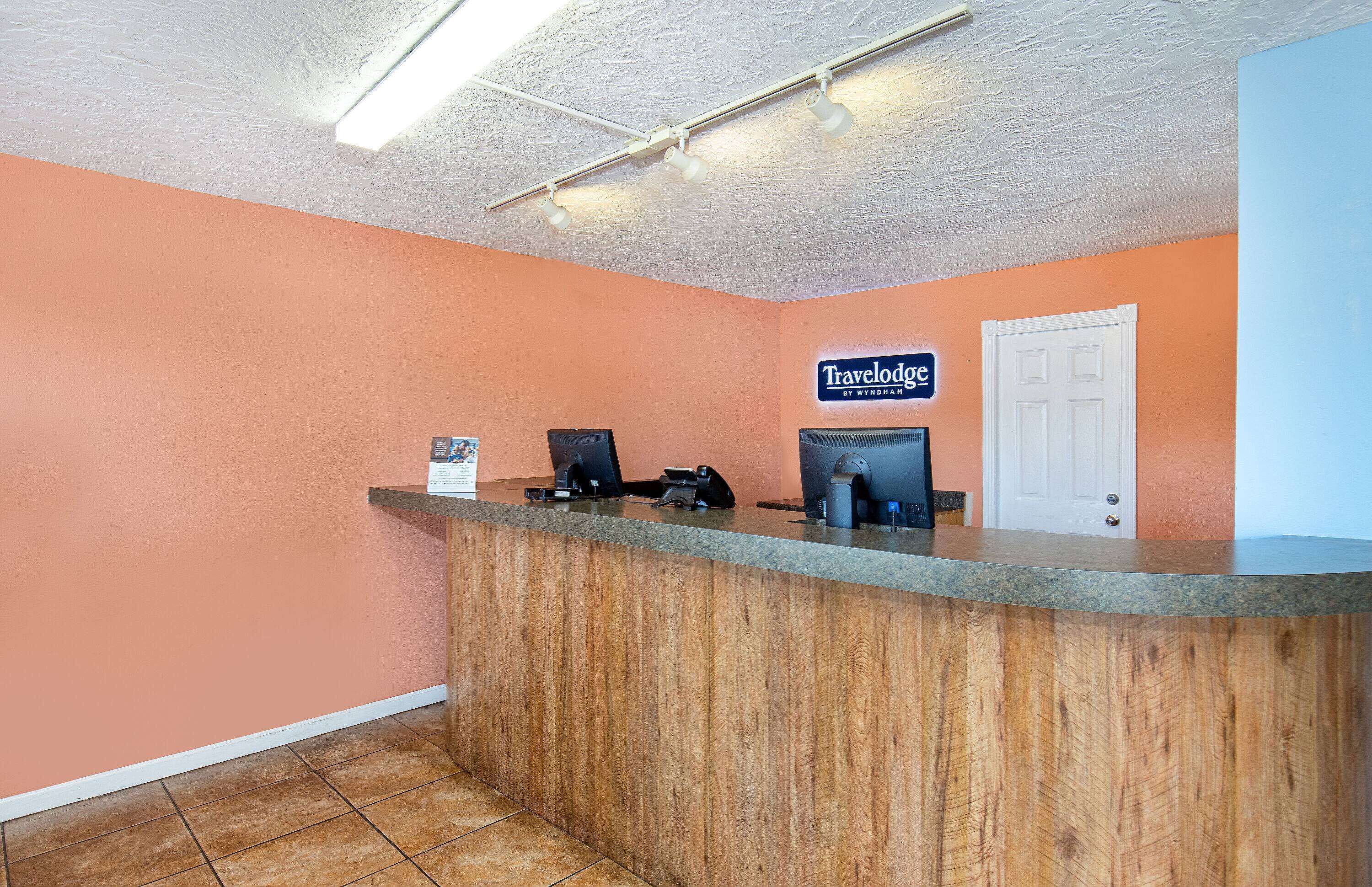 A reception desk with a wooden counter, a sign for 'Travelodge by Wyndham', and a closed door in the background.