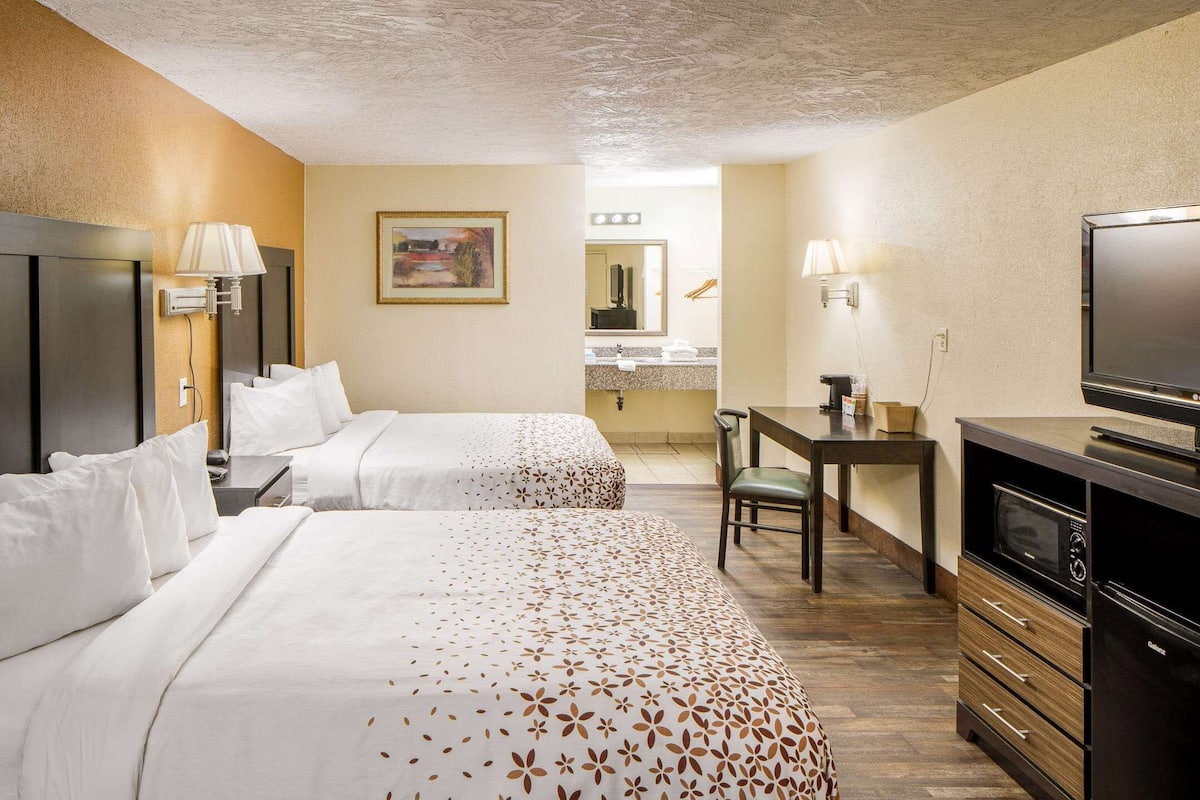 Habitación de hotel con dos camas, un escritorio, televisor y kitchenette.