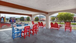 An outdoor patio with red and blue Adirondack chairs, a white table, and a view of the cityscape. - Americana Inn, a Travelodge by Wyndham (Pigeon Forge)