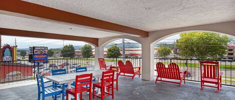 An outdoor patio with red and blue Adirondack chairs, a white table, and a view of the cityscape.