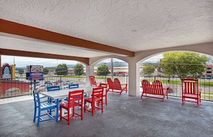 An outdoor patio with red and blue Adirondack chairs, a white table, and a view of the cityscape.