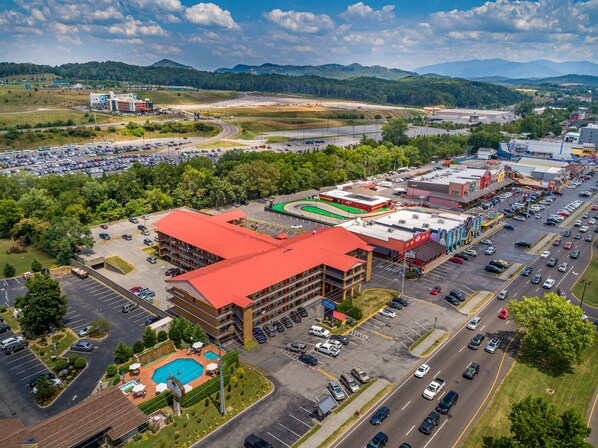 A multi-story hotel with a red roof, a swimming pool, and a parking lot. - Americana Inn, a Travelodge by Wyndham (Pigeon Forge)