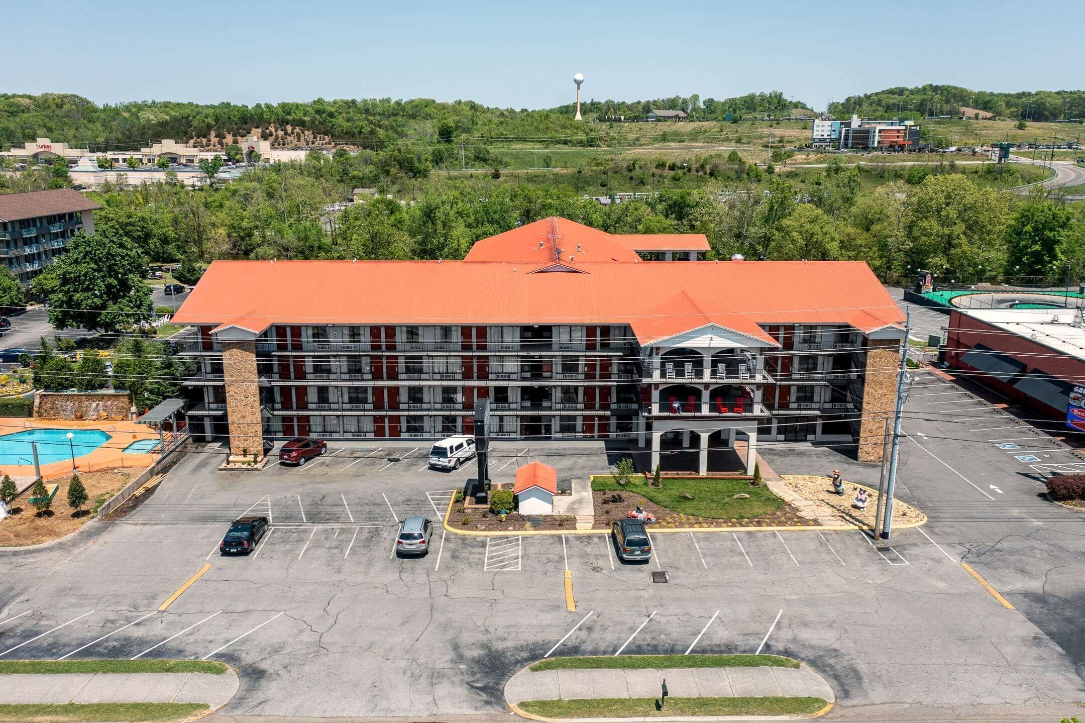 A large hotel with a red roof, multiple floors, and a parking lot with several cars.