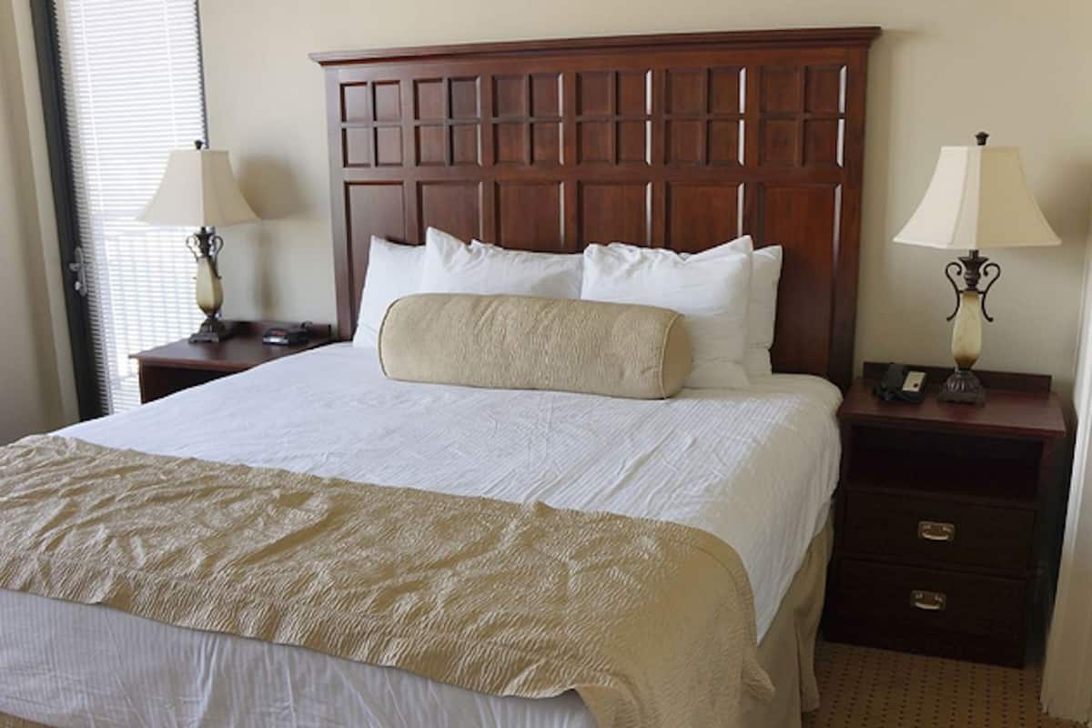 A neatly made bed with a wooden headboard, two bedside tables with lamps, and a carpeted floor.