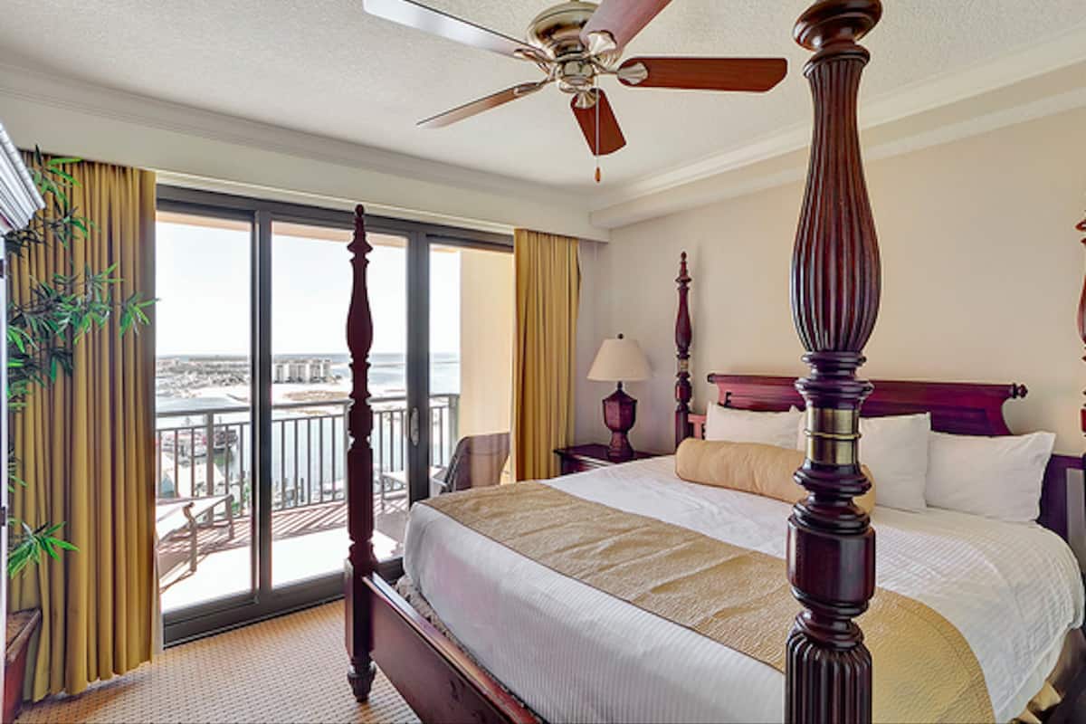 A hotel room with a large bed, a ceiling fan, a balcony with a view, and a large window.