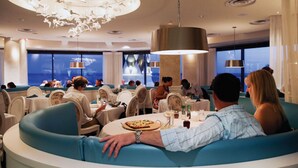Een modern restaurant met ronde tafels en blauwe zittingen met kussens.