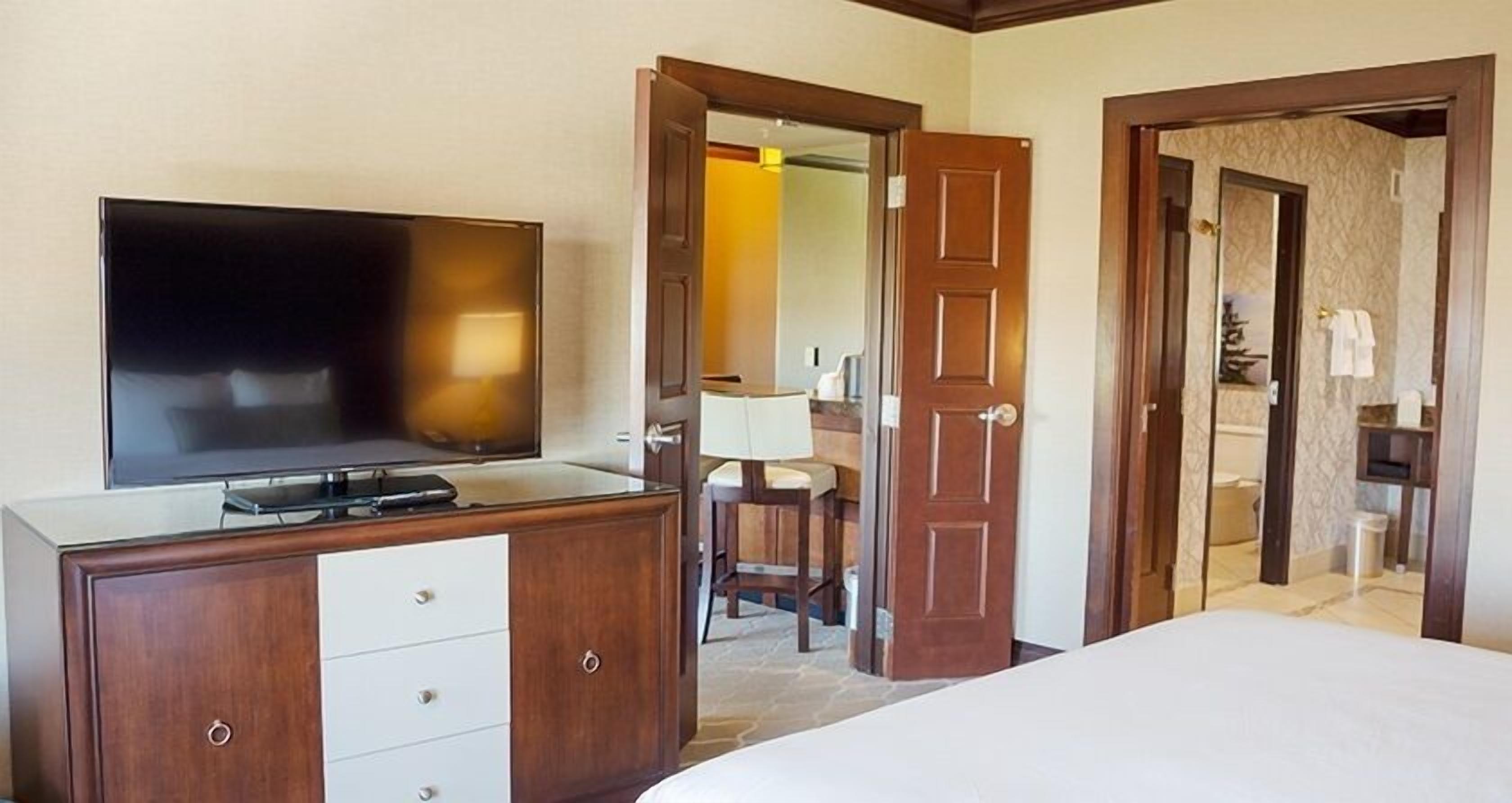 A hotel room with a TV on a wooden dresser, a bed, and two doors leading to other rooms.
