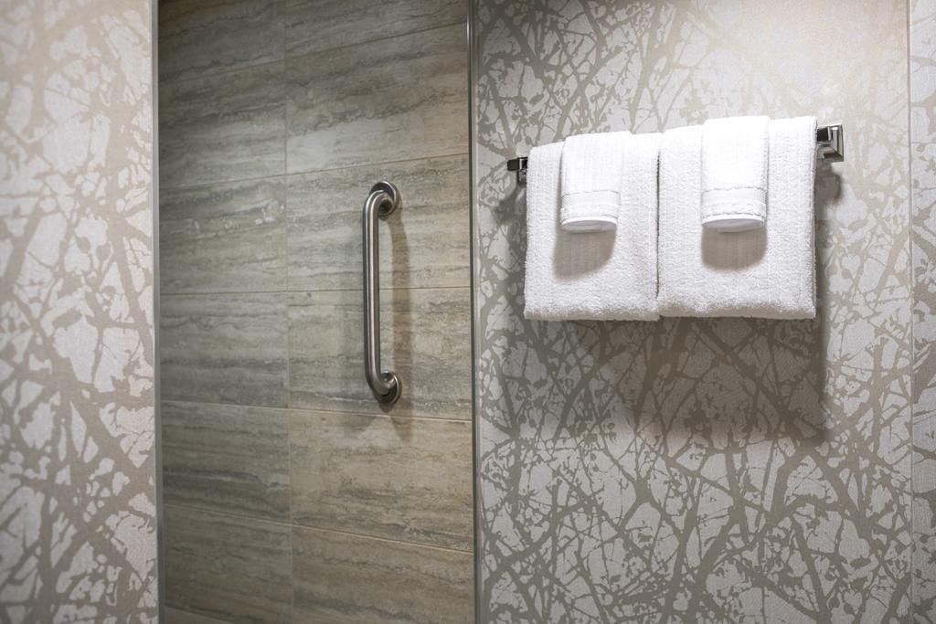 A bathroom with a wooden vanity, a towel rack with three white towels, and a handrail.