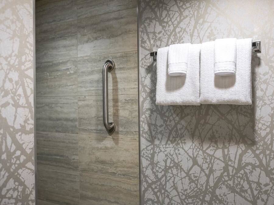 A bathroom with a wooden vanity, a towel rack with three white towels, and a handrail.