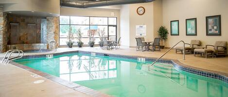 An indoor swimming pool with a stone wall, lounge chairs, and a clock on the wall.