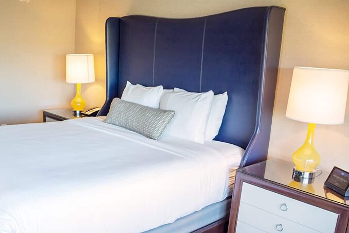 Een hotelkamer met een groot bed, twee nachtkastjes met lampen, en een nachtkastje met een telefoon en een klein tafeltje.