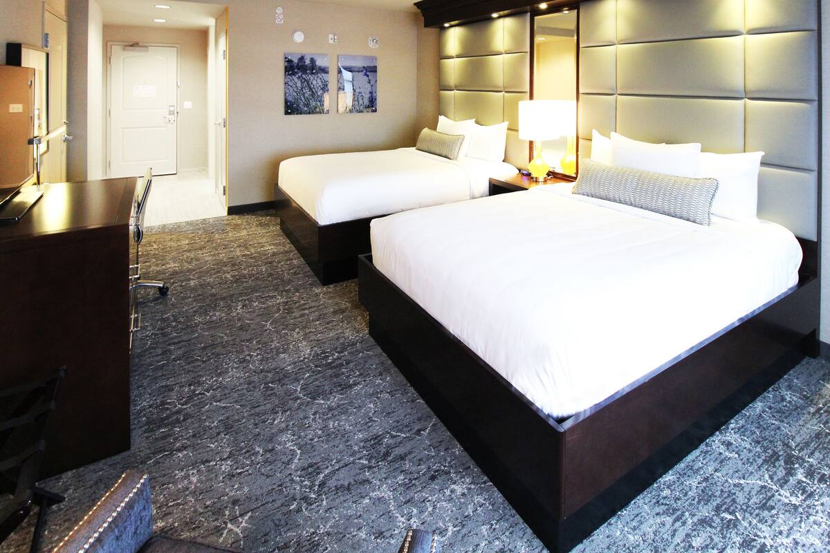Een hotelkamer met een groot bed, twee kleinere bedden, een bureau en een stoel.