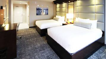 A hotel room with a large bed, two smaller beds, a desk, and a chair.