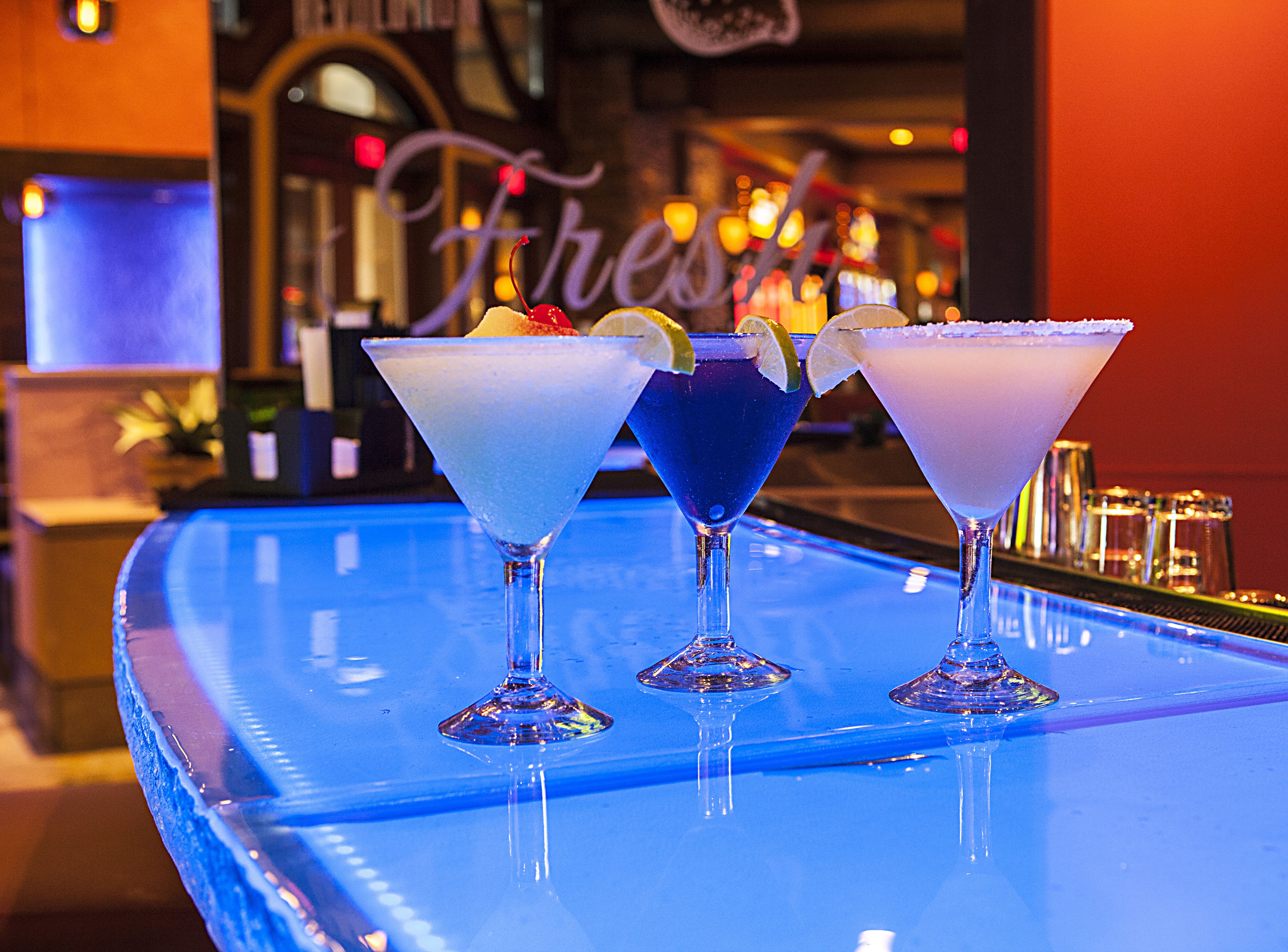 Tres copes de martini damunt una barra amb una superfície reflectant blava.