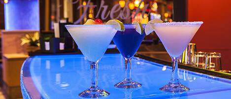 Three martini glasses on a bar counter with a blue reflective surface.