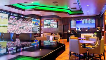 A sports bar with multiple screens displaying sports events, comfortable seating, and a counter area.