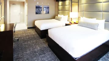 Habitación de hotel con dos camas, un escritorio y una silla. Se observa una puerta al fondo y una pared con una lámpara.