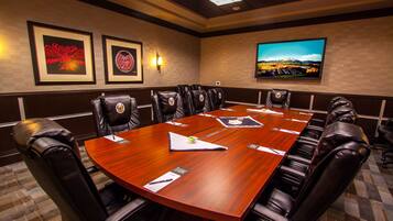 A conference room with a large wooden table, leather chairs, framed artwork on the walls, and a television displaying a scenic view.
