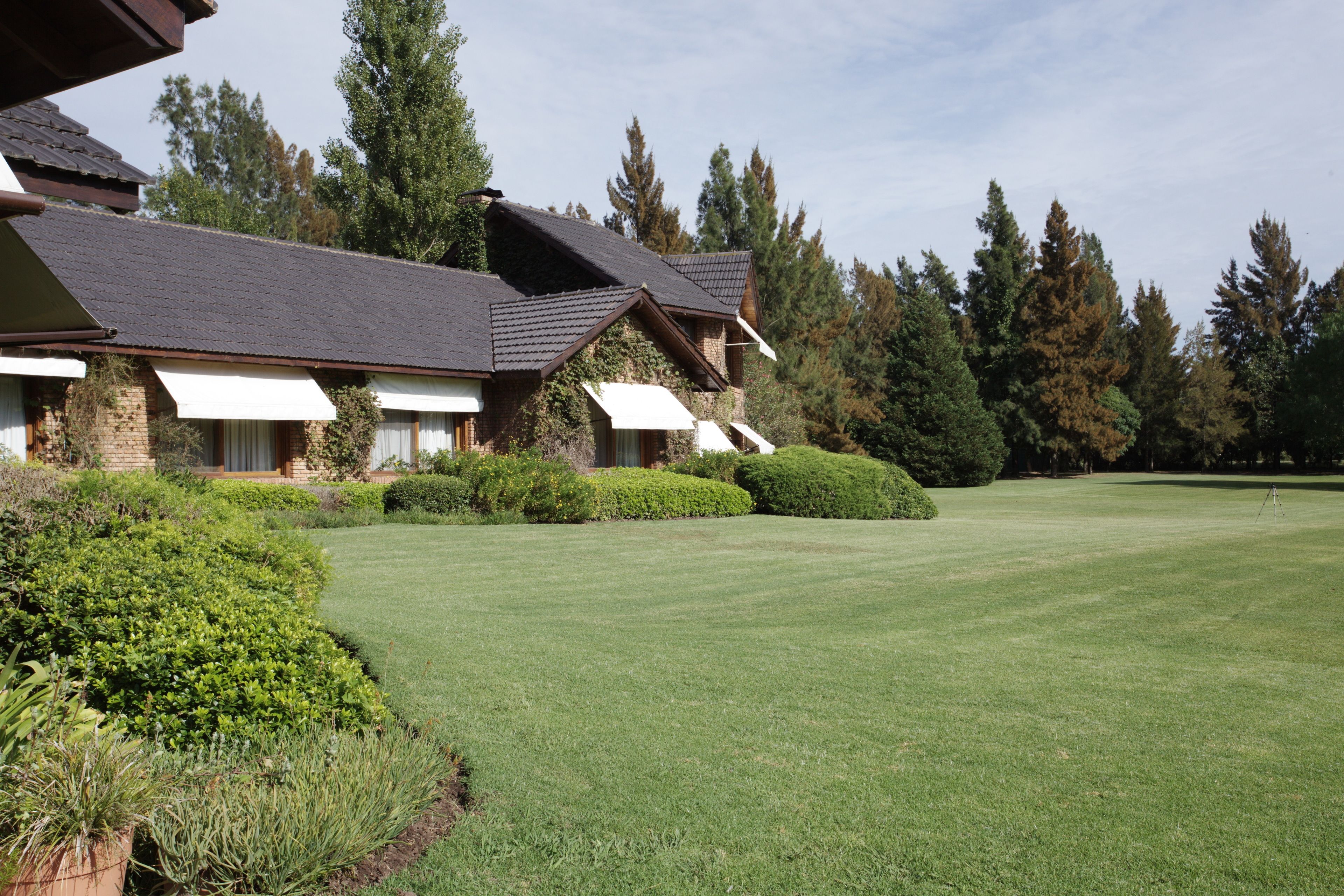 A large, multi-story building with a sloped roof, surrounded by well-maintained lawns and dense trees.