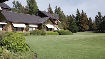 A large, multi-story building with a sloped roof, surrounded by well-maintained lawns and dense trees.