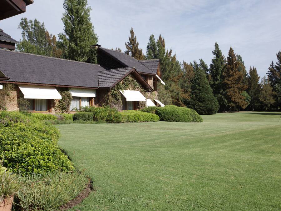 A large, multi-story building with a sloped roof, surrounded by well-maintained lawns and dense trees.