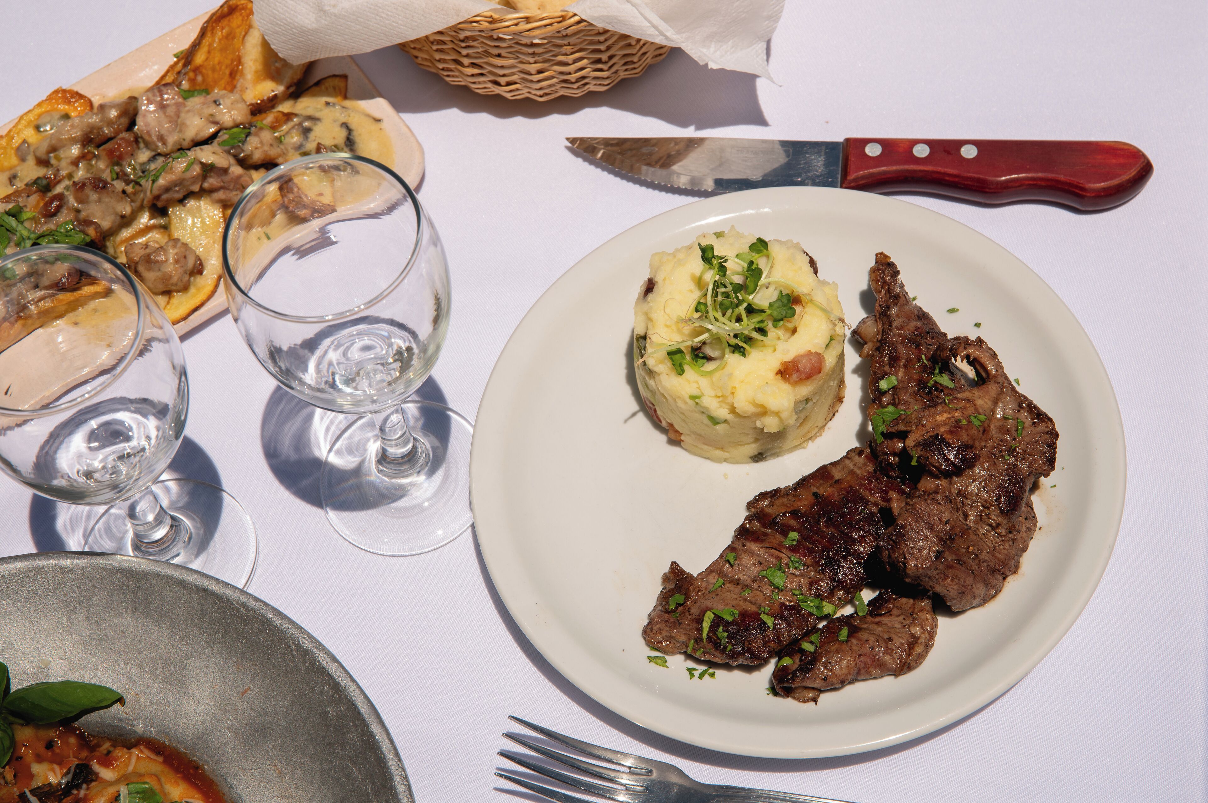 A plate with meat and mashed potatoes, two glasses of water, and a knife on a table.
