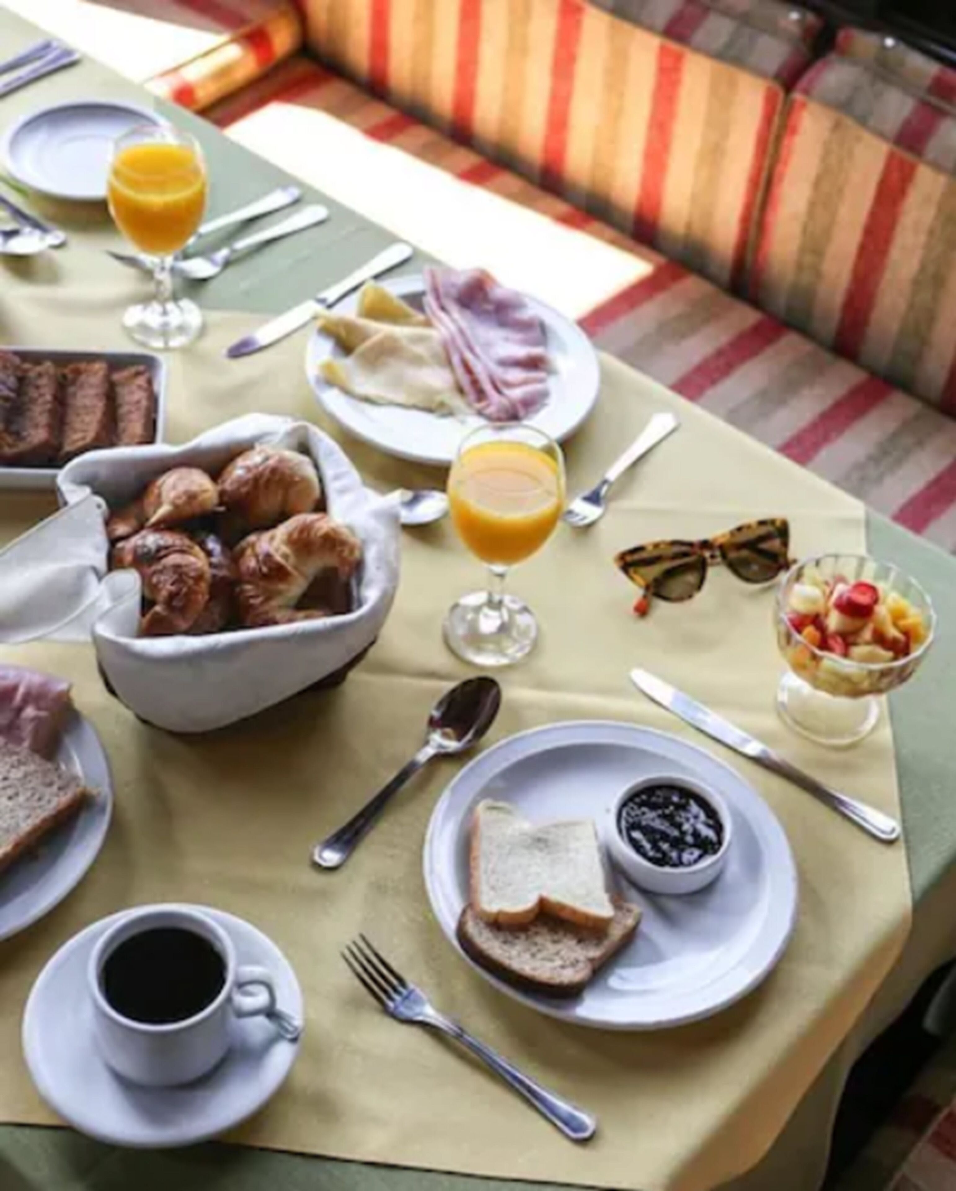 A breakfast setting with a table set for two, including plates with toast, a bowl of bread, a glass of orange juice, a cup of coffee, and a bowl of blackberries.