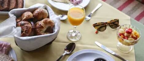 A breakfast setting with a table set for two, including plates with toast, a bowl of bread, a glass of orange juice, a cup of coffee, and a bowl of blackberries.
