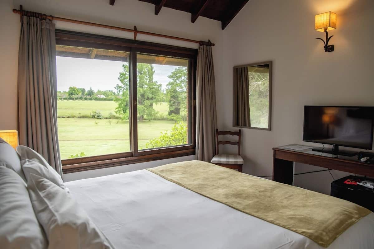 Ein Hotelzimmer mit einem Bett, einem Schreibtisch mit Fernseher, einem Sessel und einem Fenster mit Vorhängen.