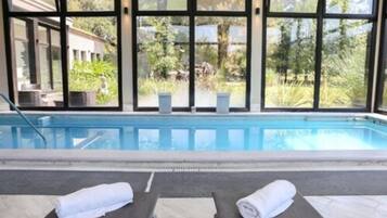 Zona de piscina con dos sillas de descanso y vistas a un edificio y follaje a través de amplios ventanales.