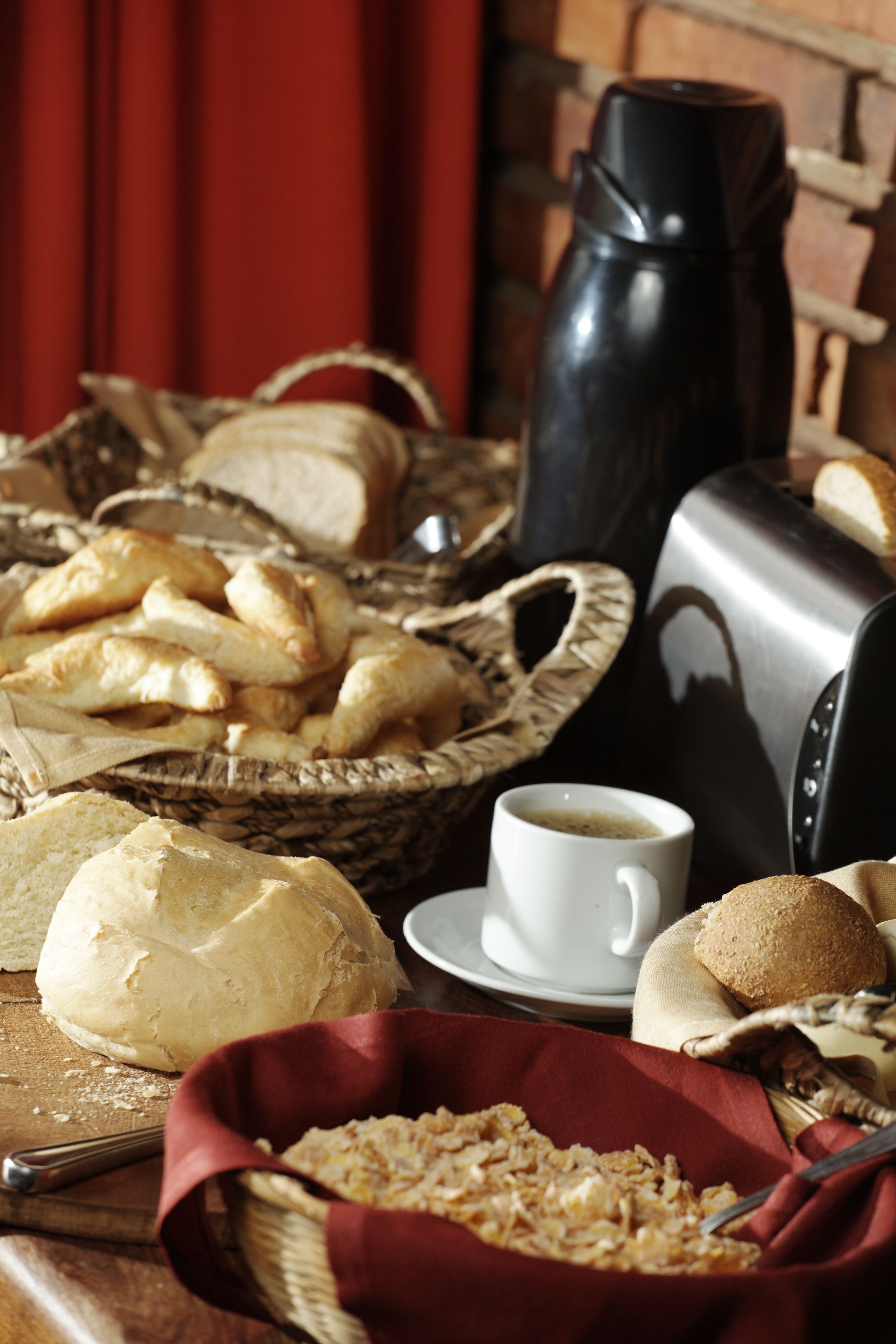 A breakfast setting with bread, pastries, a coffee pot, and a cup on a wooden table.