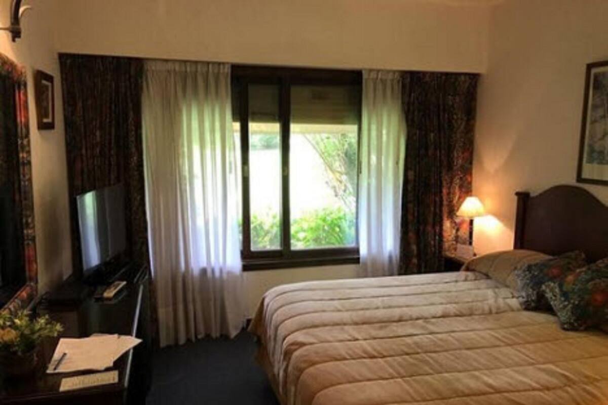 Ein Hotelzimmer mit Bett, Fernseher, Schreibtisch mit Lampe und einem Fenster mit Vorhängen.