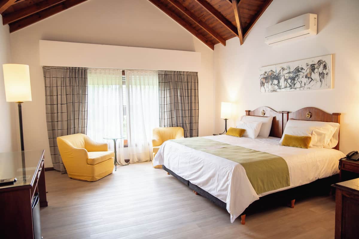 Ein Hotelzimmer mit einem Bett, zwei Stühlen, einem Schreibtisch und einer Klimaanlage.