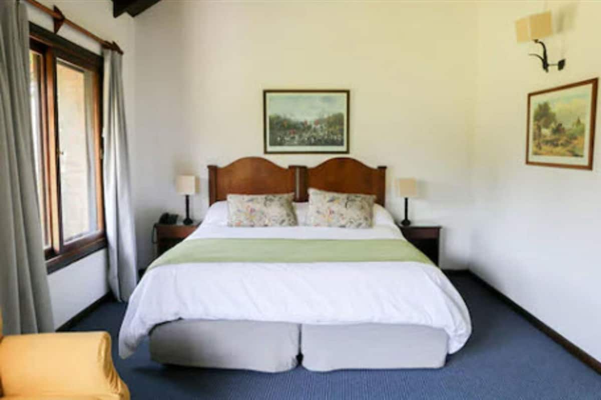 Ein Hotelzimmer mit einem großen Bett, zwei Nachttischen, einem Fenster mit Vorhängen und zwei Wandlampen.