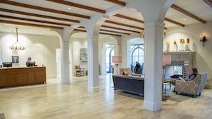 Un vestíbulo espacioso con techos altos, vigas de madera y una zona de estar central con un sofá y sillones.
