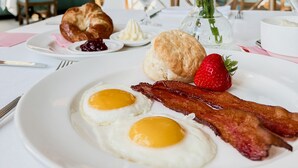 Un desayuno con huevos, tocino, un croissant y una fresa sobre un plato blanco.